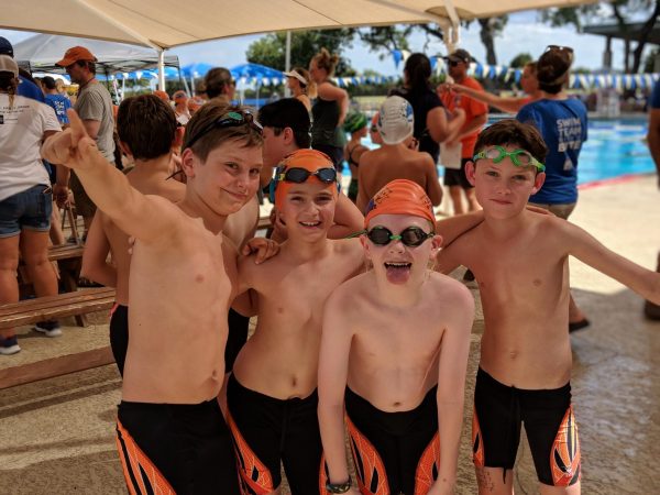 A group of 4 boys on the Piranhas swim team smile together.