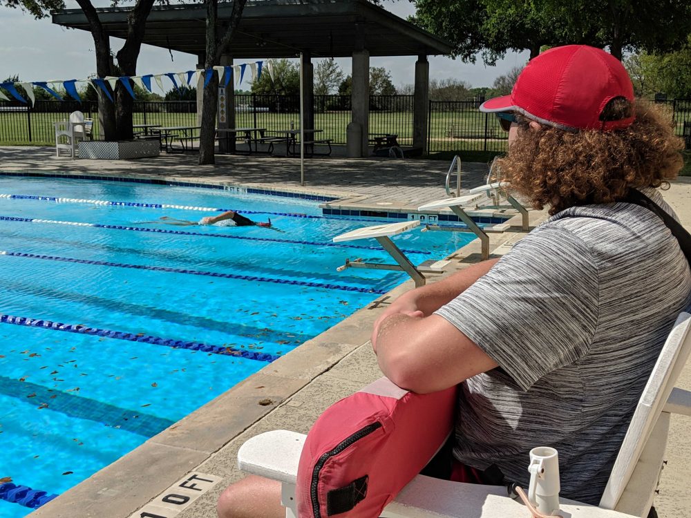 A lifeguard wearing a red hat watches a swimmer in the lap lane.
