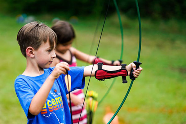 A boy and girl practice shooting a bow and arrow during archery at JCamps.