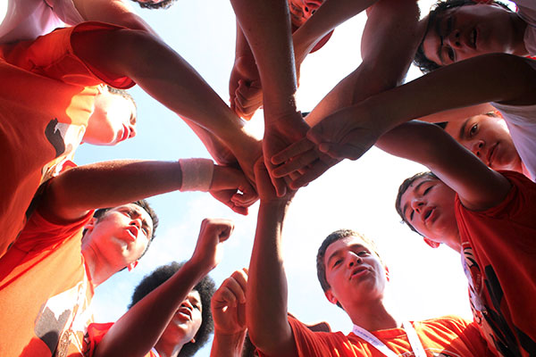 Teens at Maccabi wearing orange shirts with hands together as a team