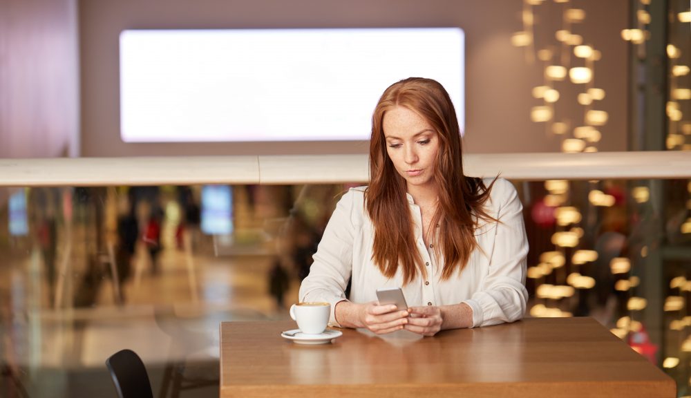 A woman on her iPhone is sitting at a table wondering the best way to give