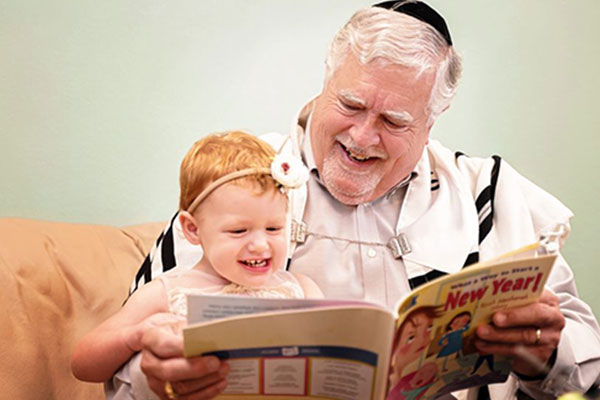 A grandfather reads a Rosh Hashanah book to his toddler granddaughter