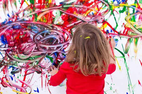 A young girls paints abstract art on a wall