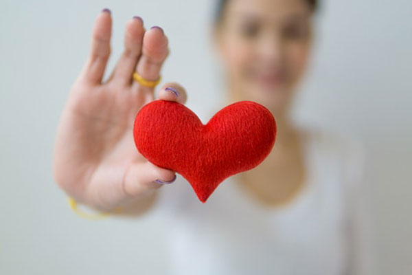 Close up of woman's hands holding a fuzzy red heart over a wood table