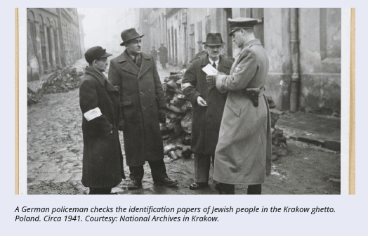 A German policeman checks the identification papers of Jewish people in the Krakow ghetto. Poland. Circa 1941. Courtesy: National Archives in Krakow.