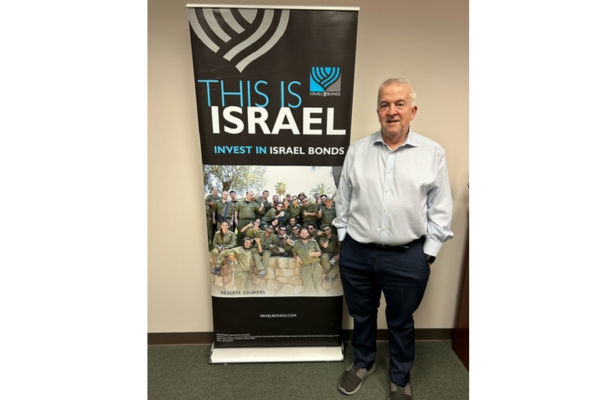 Israel Bonds Houston Representative Steve Landis standing proudly in front of an Israel Bonds banner. Courtesy: Israel Bonds